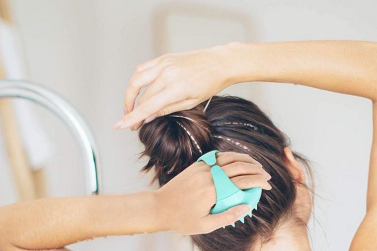 Green scalp massager brush used to massage wet hair at the scalp
