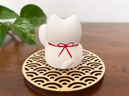 White Maneki Neko cat figurine with red bow on round wave-pattern base