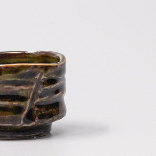 Ceramic sake cup side with cutout pattern and dark brown-green glaze