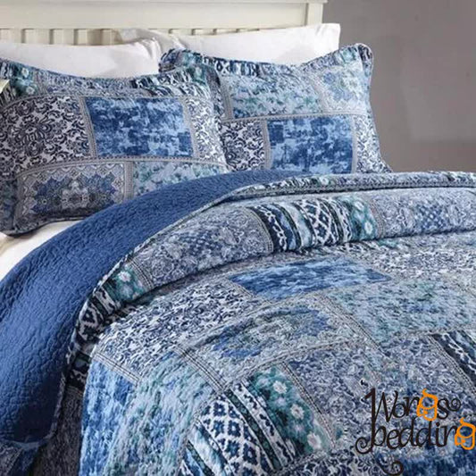 Blue quilt coverlet with geometric patchwork edge and patterned pillow shams