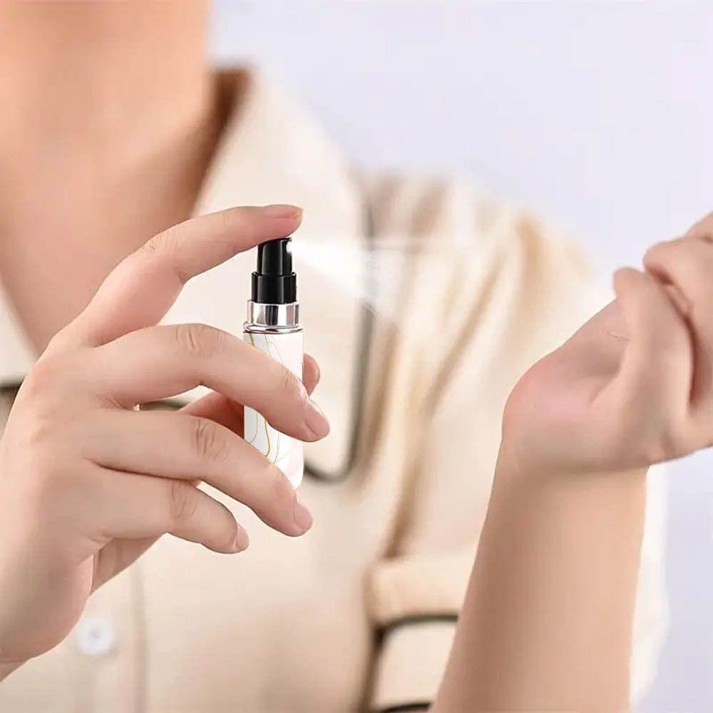 White marble travel perfume atomizer being sprayed by hands, black pump sprayer