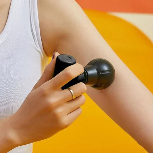 Mini massage gun with black grip and round head, held against an arm