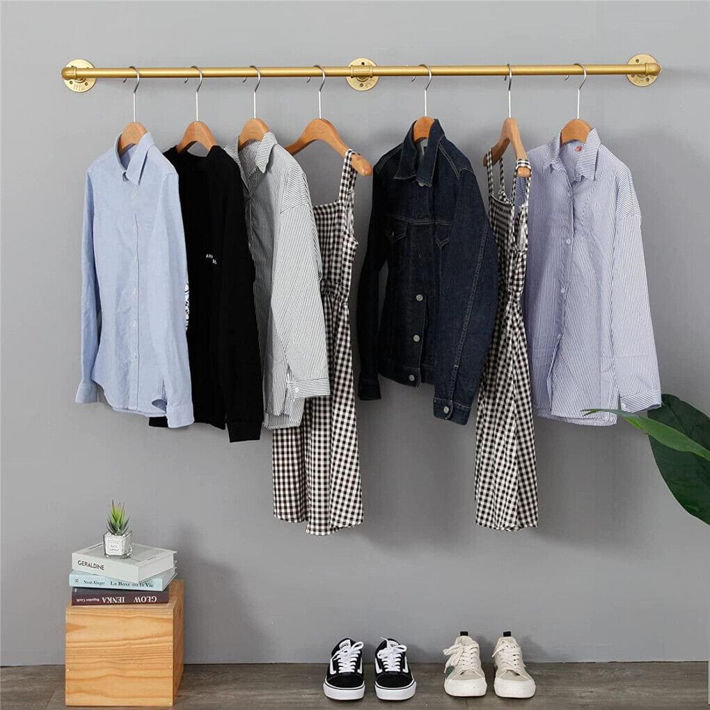 Gold wall-mounted clothes rail with hangers and shirts, jackets, and dresses in mixed tones