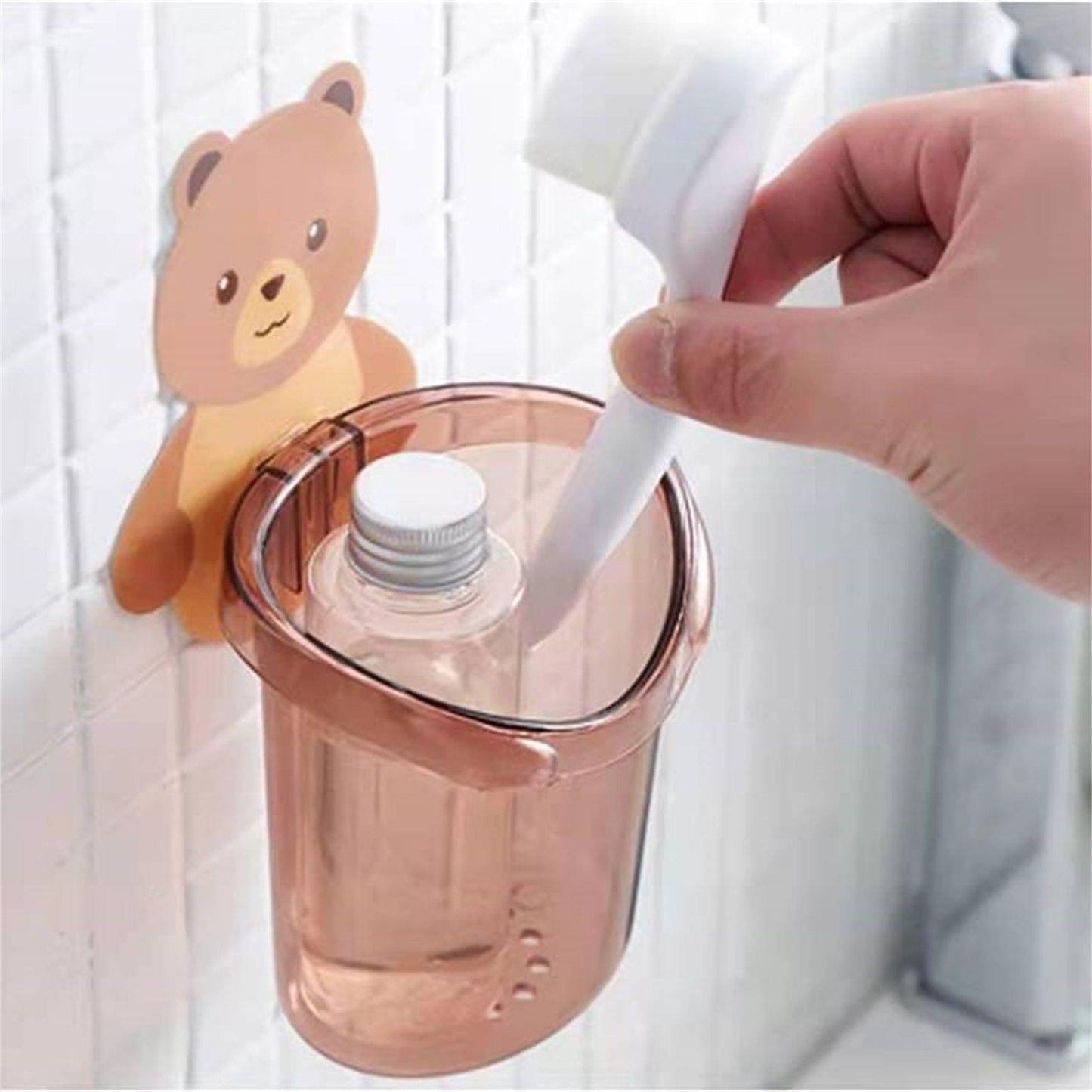 Wall-mounted bear toothbrush holder with clear cup, shown with hand inserting