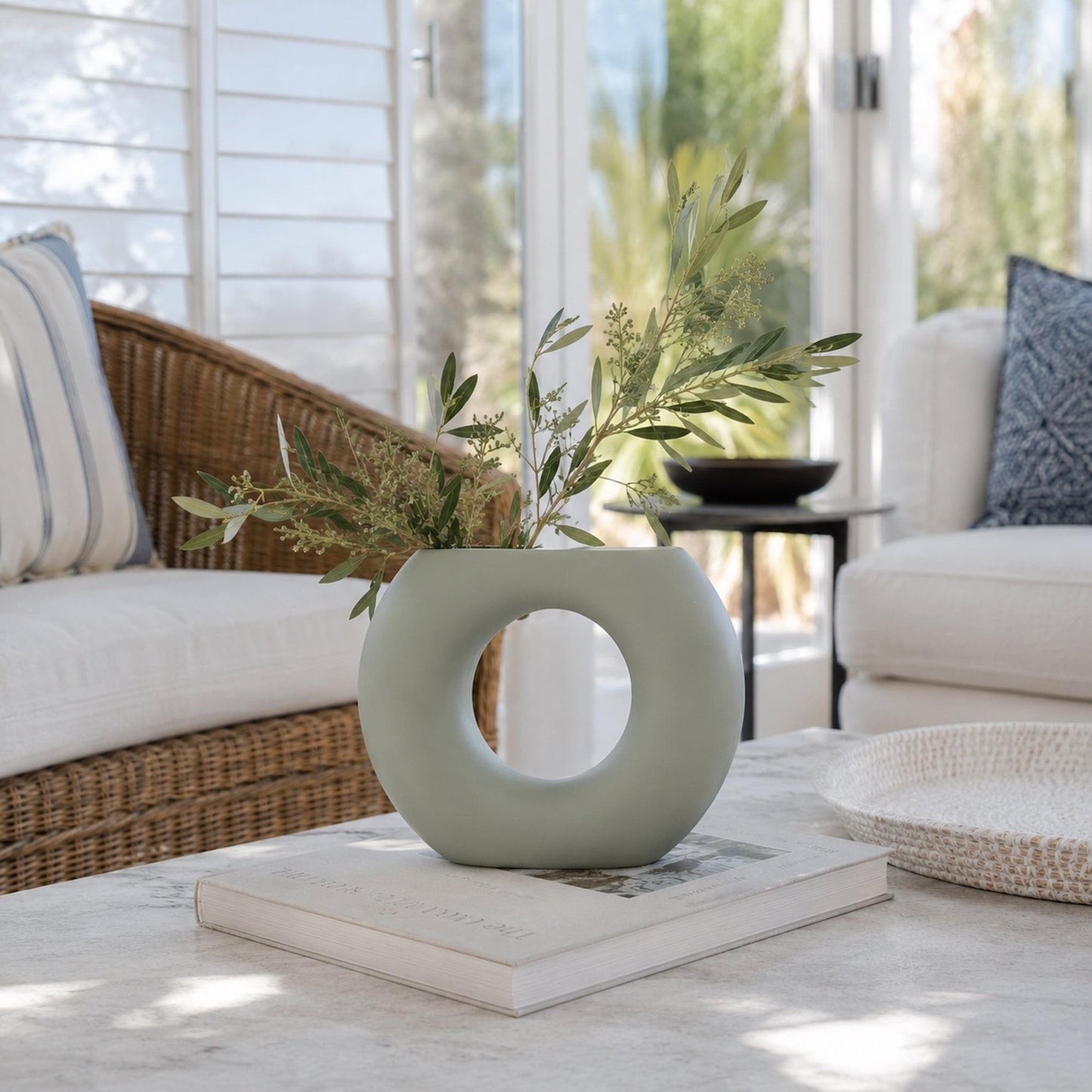 Sage grey ceramic vase with oval cutout and floral stems on a tabletop