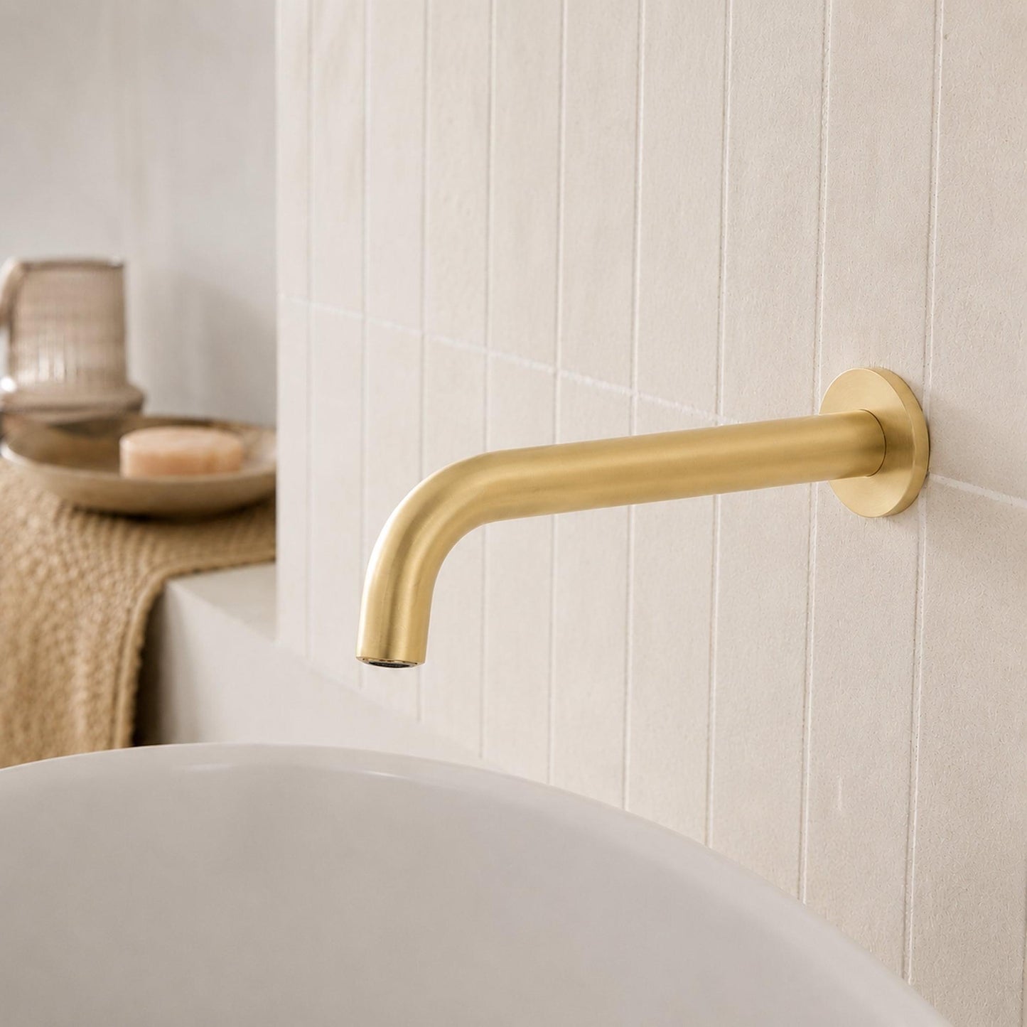 Brushed brass curved wall spout with round escutcheon on tiled wall
