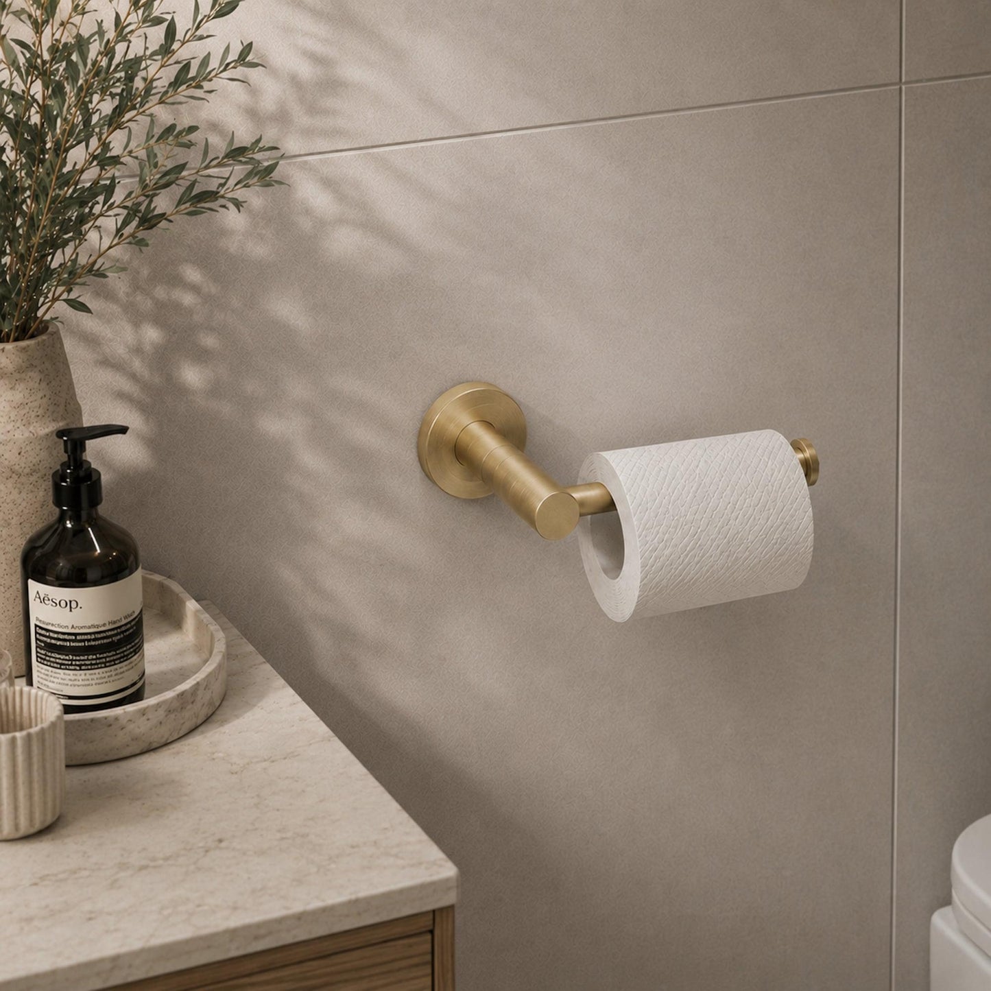 Brushed brass toilet roll holder holding a paper roll on wall
