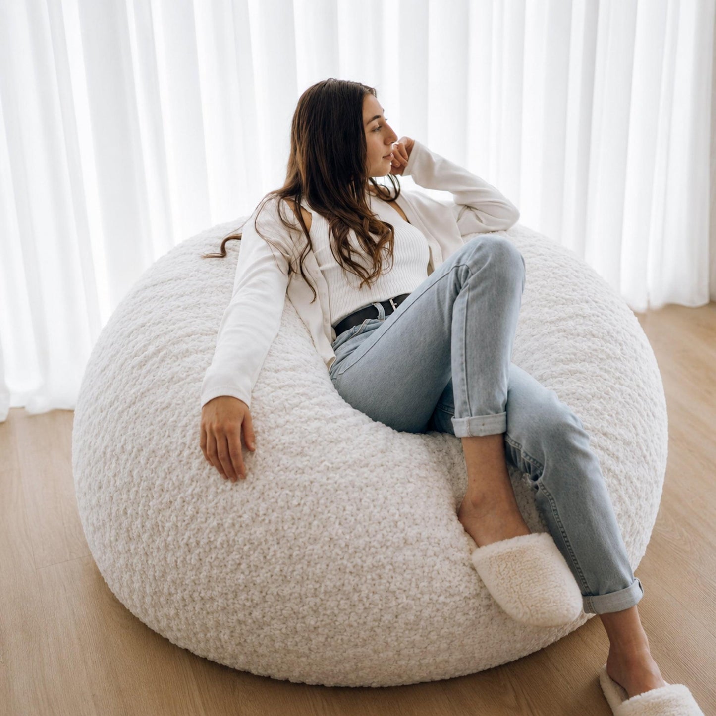 White plush bean bag chair with rounded back, adult relaxing with legs up