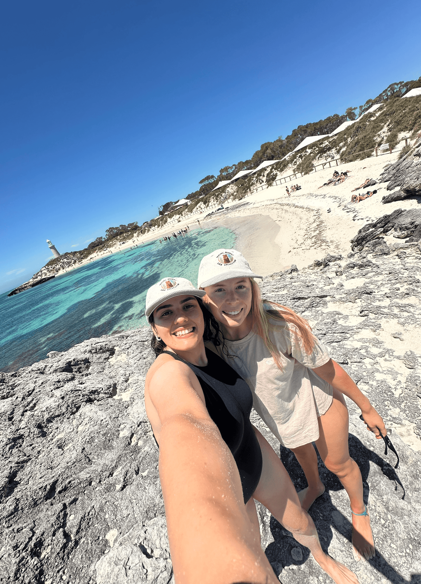 White ribbed cap with quokka logo patch worn in sunny outdoor beach scene.