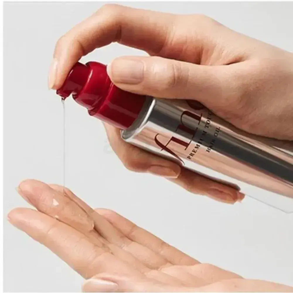 Hand holding red cap hair oil bottle, dispensing onto palm