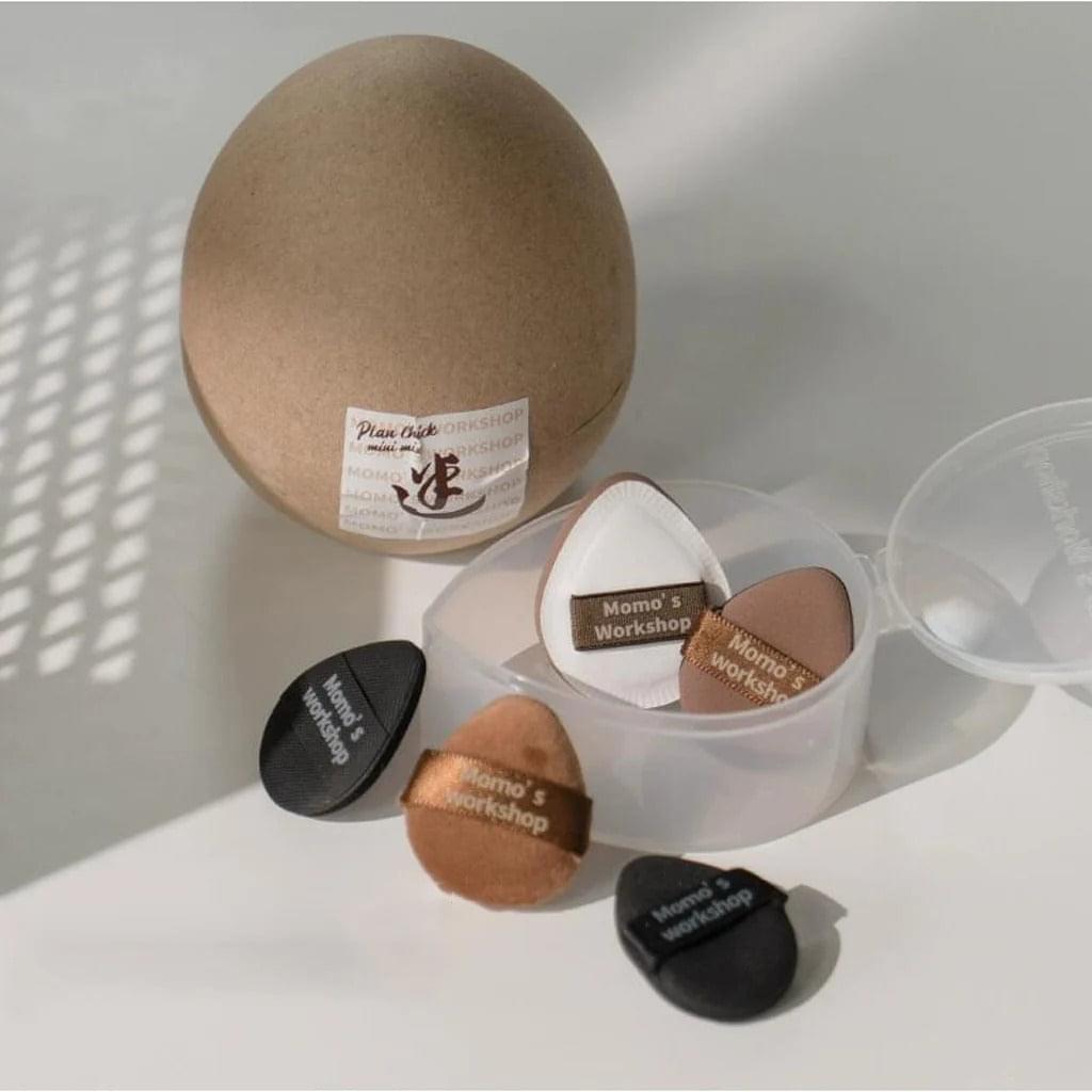Mini makeup puffs in clear container with beige pouch; black, brown, and white sponges