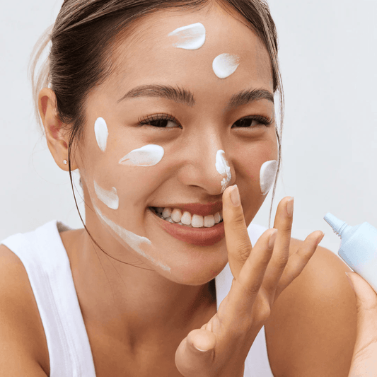 Skincare model with white sunscreen swatches and a light blue SPF tube