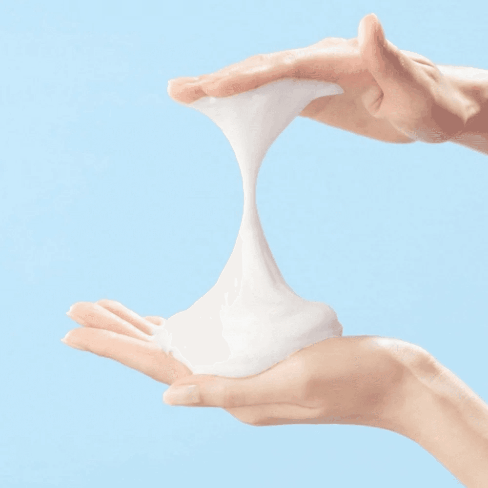 White facial cleanser foam dispensed between hands.