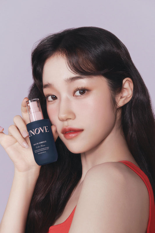Silk hair oil essence bottle held beside woman's cheek, red top