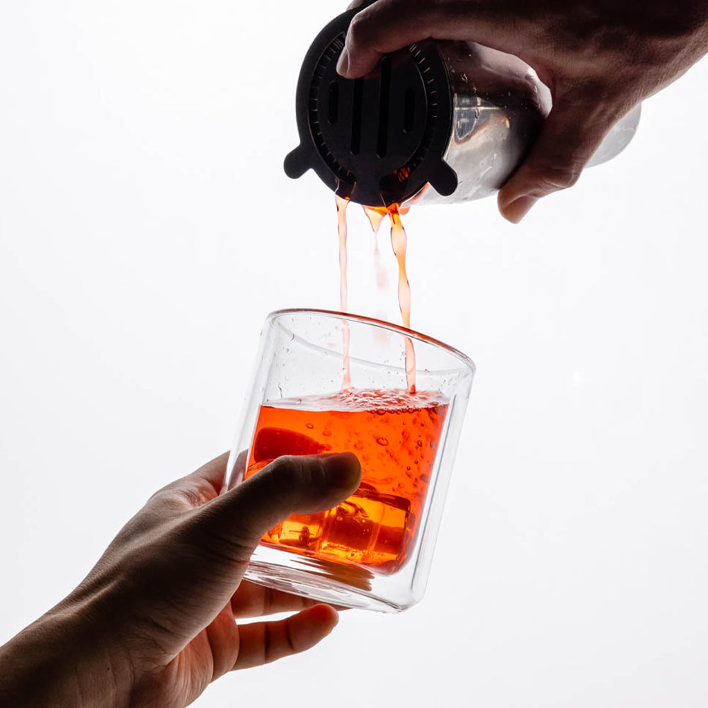 Clear glass rocks tumbler being filled with amber liquid from a pour spout