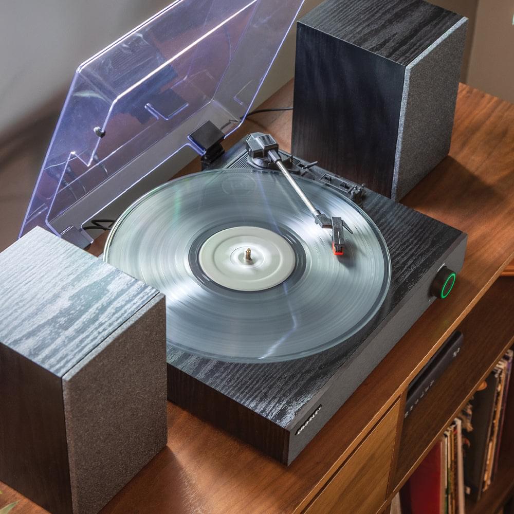 Black turntable with open clear dust cover, spinning vinyl, and stereo speakers