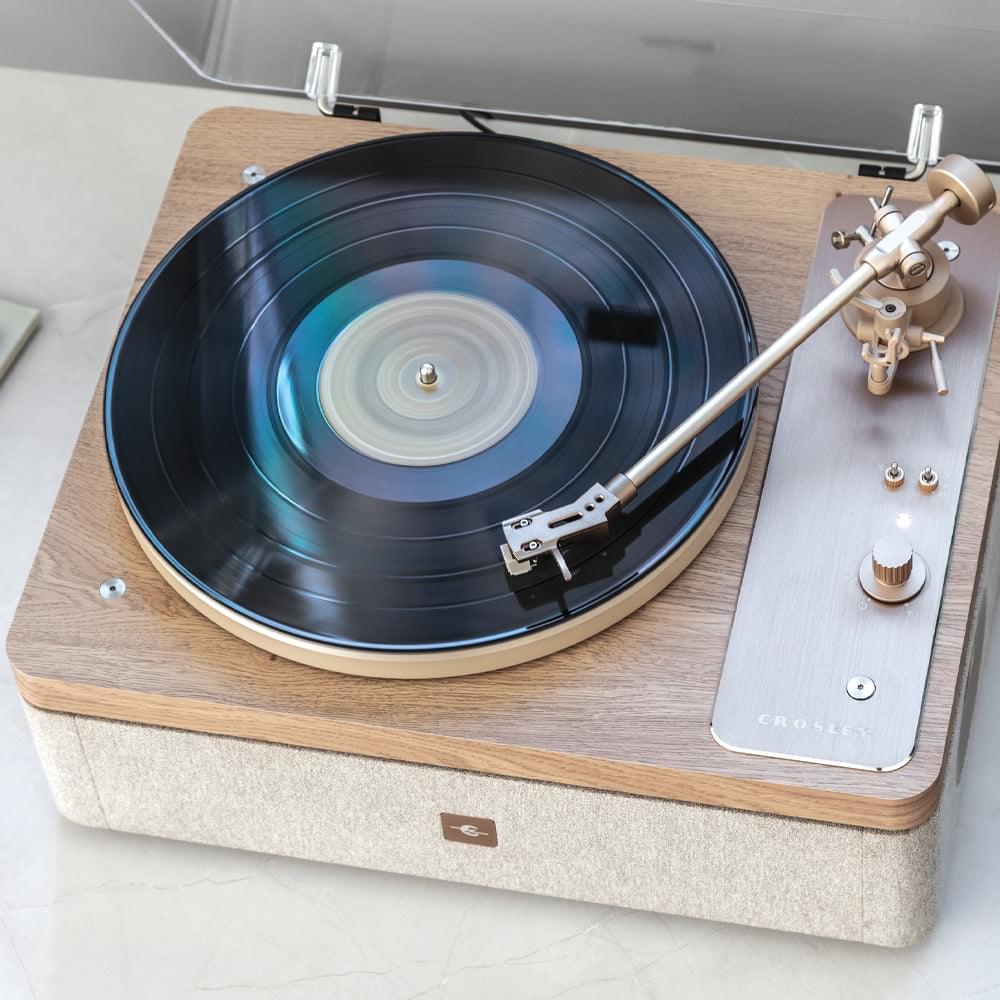Record player with spinning vinyl, natural wood deck, and tonearm over controls