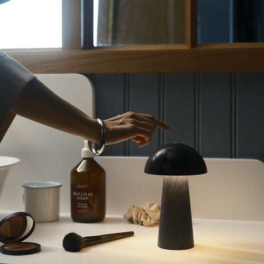 Portable rechargeable lamp with black dome shade on tabletop, wood base