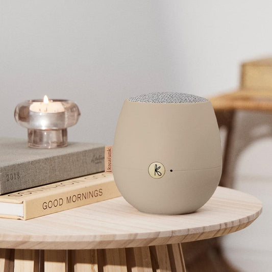 Ivory sand Bluetooth speaker on a table, fabric top and side K logo