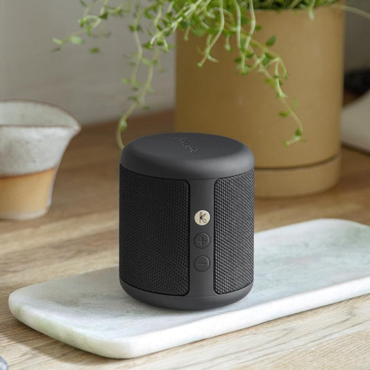 Black Bluetooth speaker on a round base, showing side speaker grille and buttons