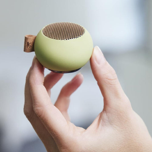 Dusty green mini Bluetooth speaker held in hands, showing top mesh grille and strap