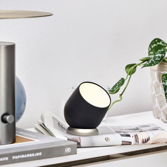 Black rechargeable table lamp on tabletop, with warm light through the top