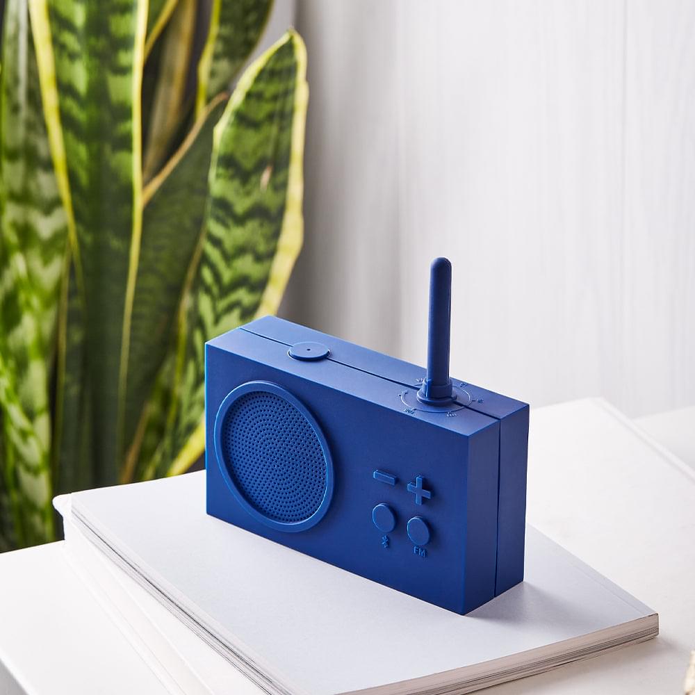 Dark blue portable radio speaker on white surface with antenna, grille, and plus/minus controls
