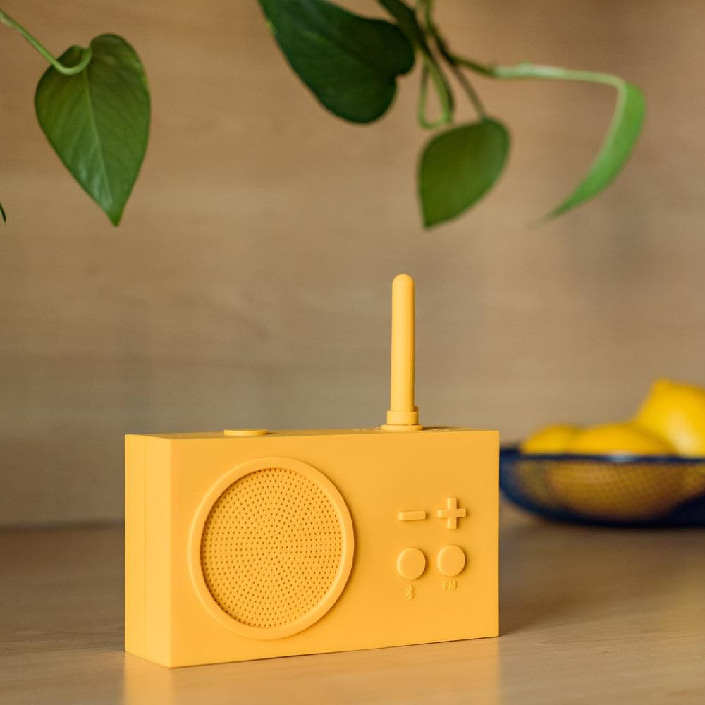 Yellow portable FM radio speaker with antenna, front grille, and volume buttons