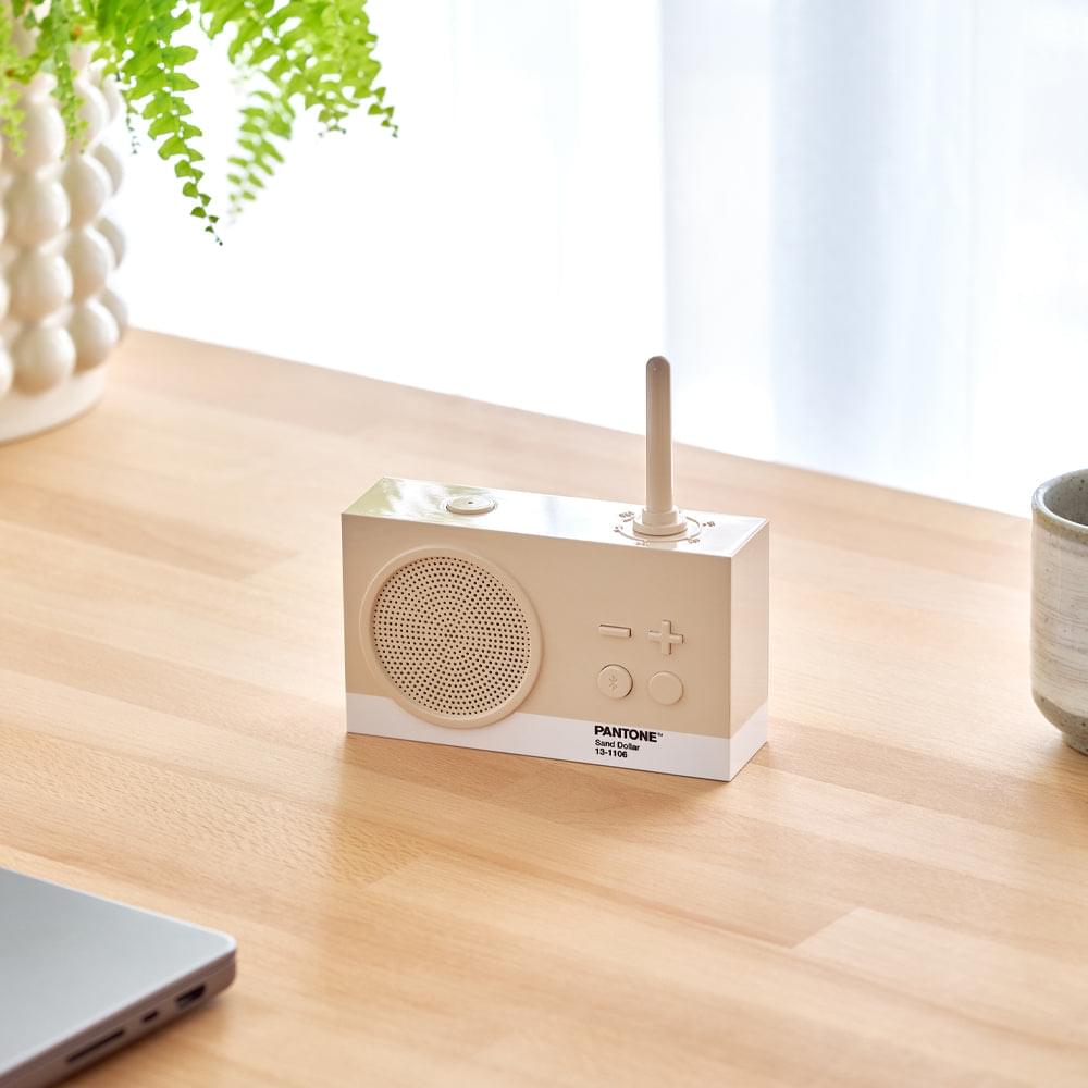Sand portable radio speaker with antenna, grille, and buttons on a wooden table