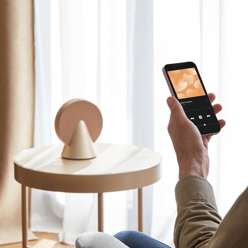 Gold conic Bluetooth speaker, phone control shown with hand reaching