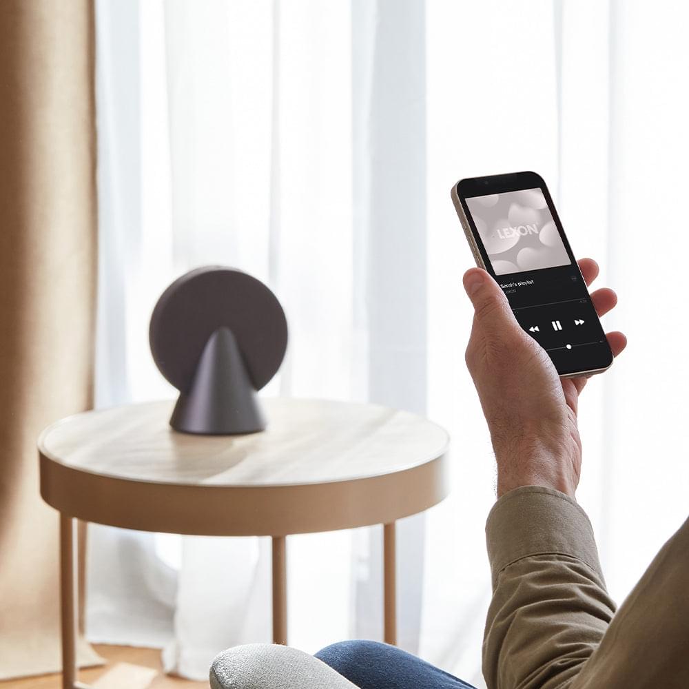 Grey conical Bluetooth speaker with fabric grille controlled from a smartphone