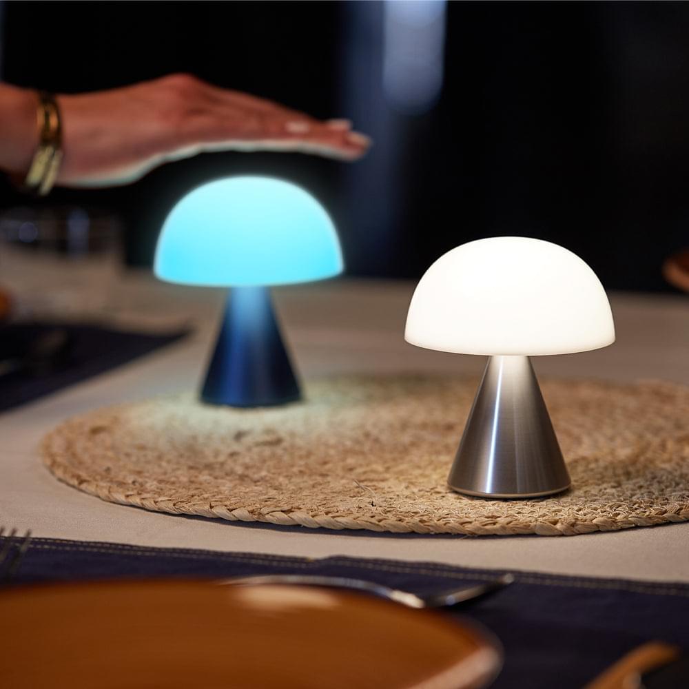 Two portable LED lamps with glowing white domes and polished aluminum cone bases on rug