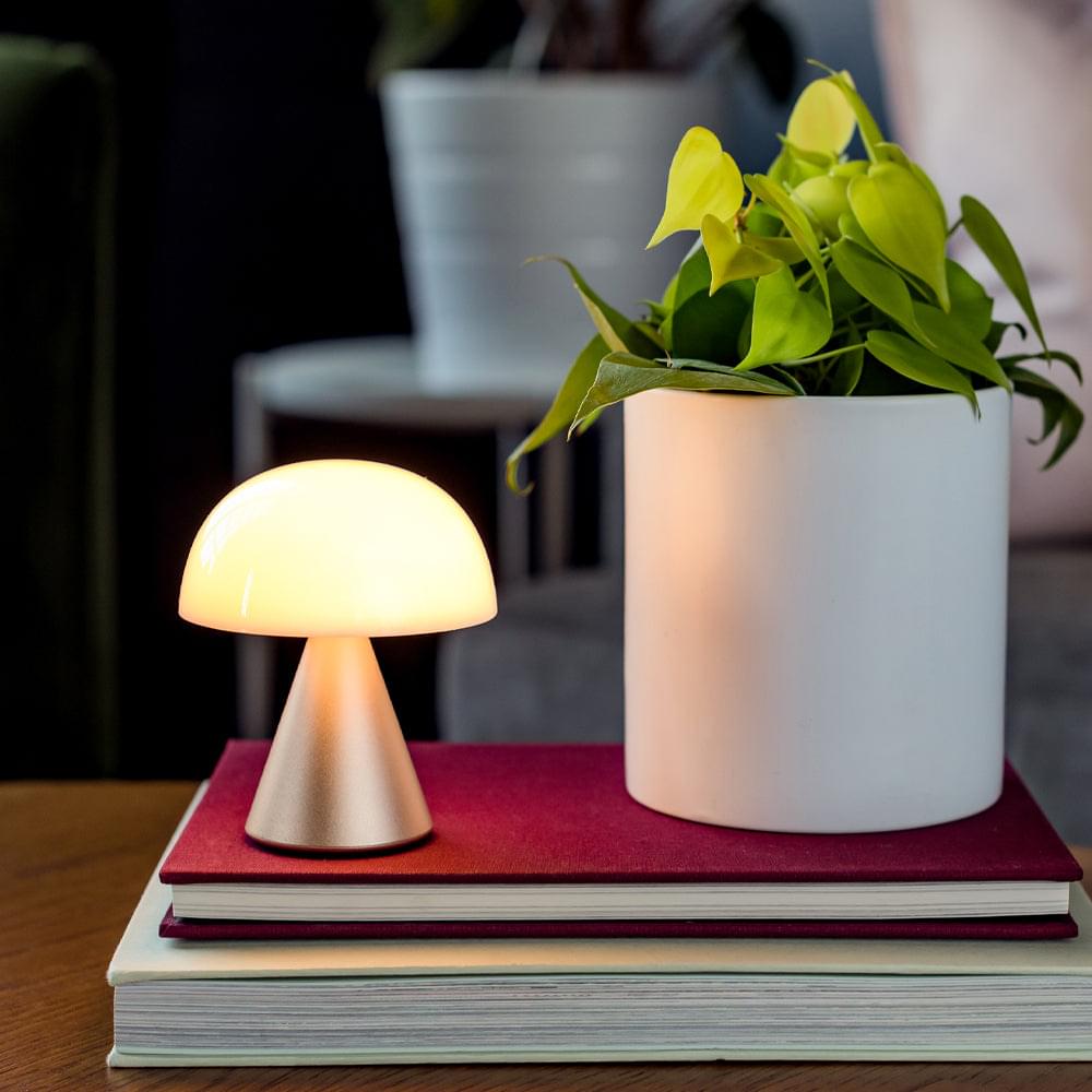 Portable LED lamp with glowing white dome shade and gold-toned base on book stack.