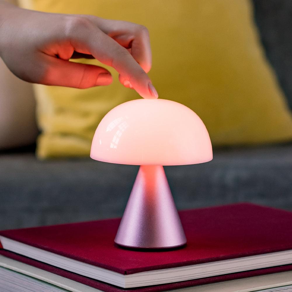 Portable LED lamp with pink glowing dome and rose-gold base, hand pressing top