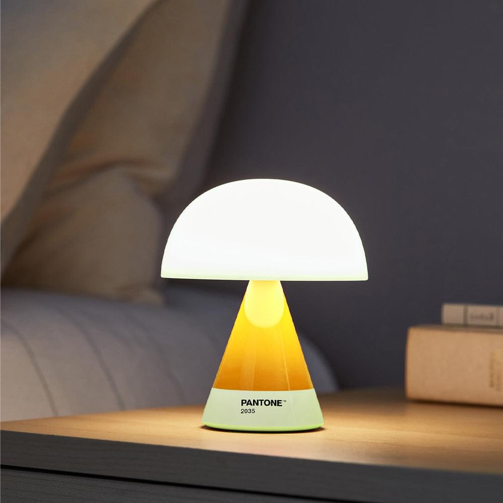 Portable LED lamp on bedside table with white dome shade and yellow base, PANTONE 2035.
