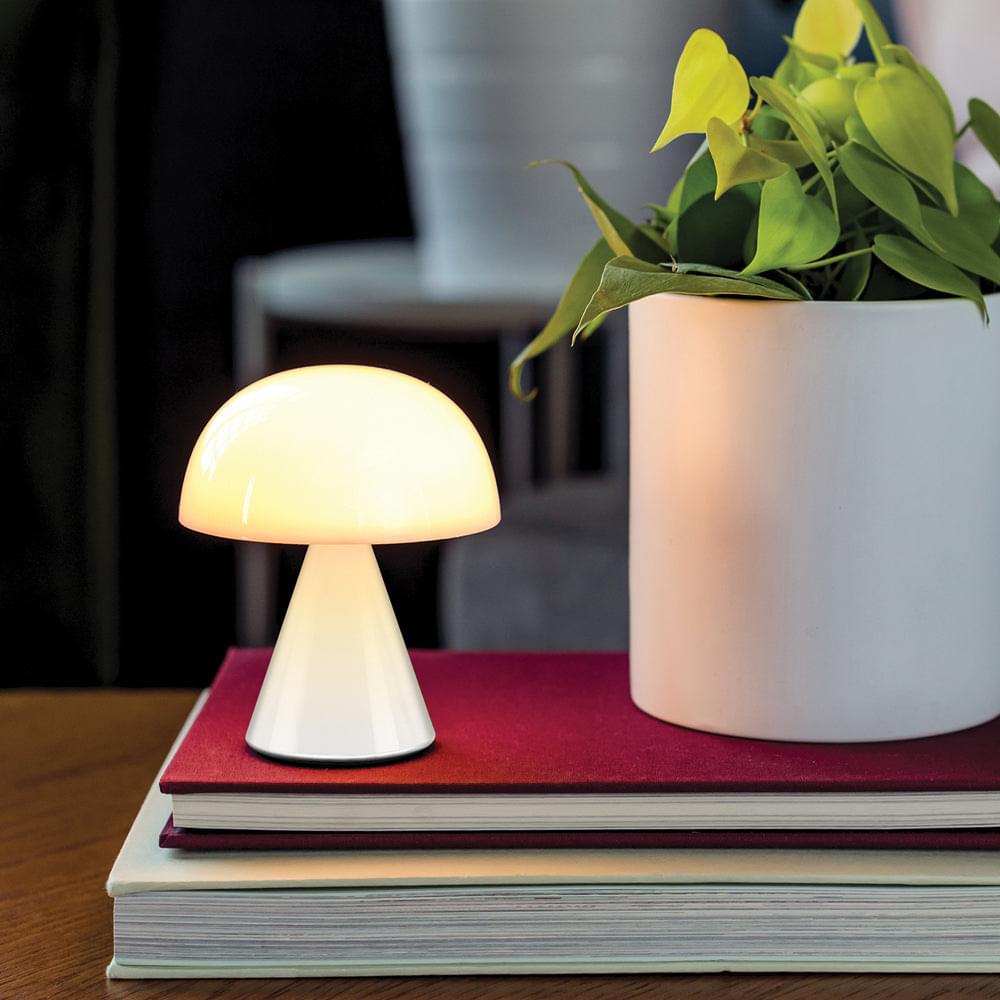 Portable LED table lamp glowing warm with white dome shade and base.