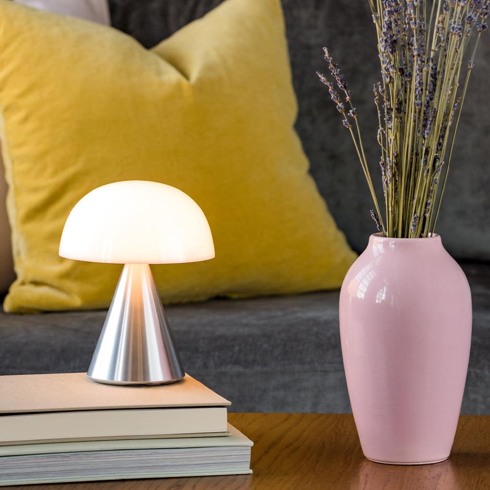 Portable LED lamp on side table with glowing white dome shade and aluminum base.