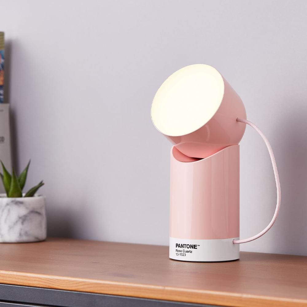 Rose pink portable LED lamp with glowing head on shelf and power cable