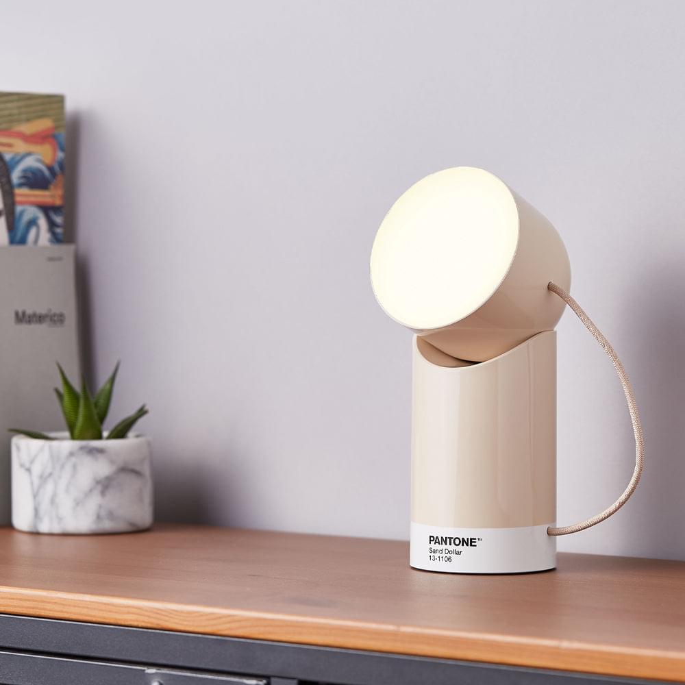 Sand portable LED lamp on sideboard, round glowing head atop cylindrical base