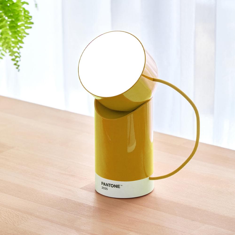 Yellow portable LED lamp on a table with raised round shade, cable loop, base labeled PANTONE