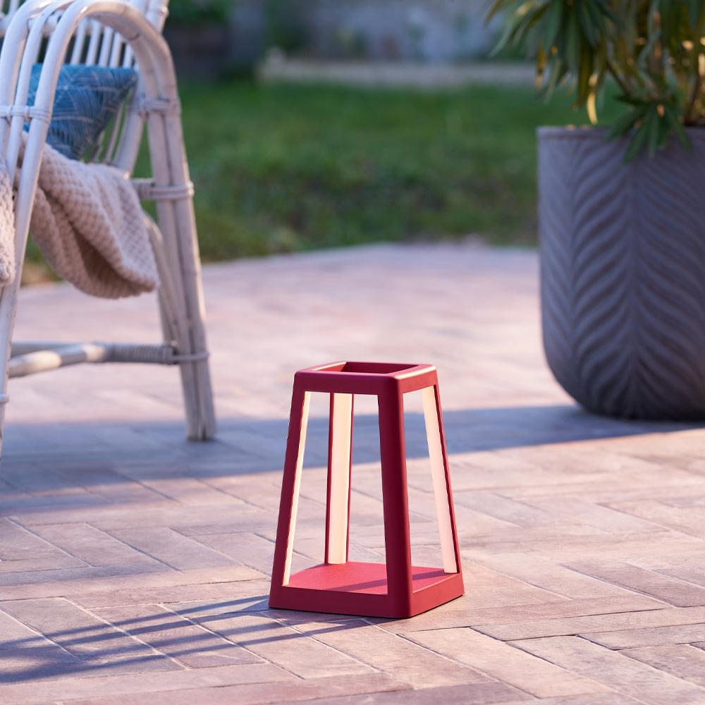 Red portable lantern lamp standing on patio tiles, open frame with white light bars