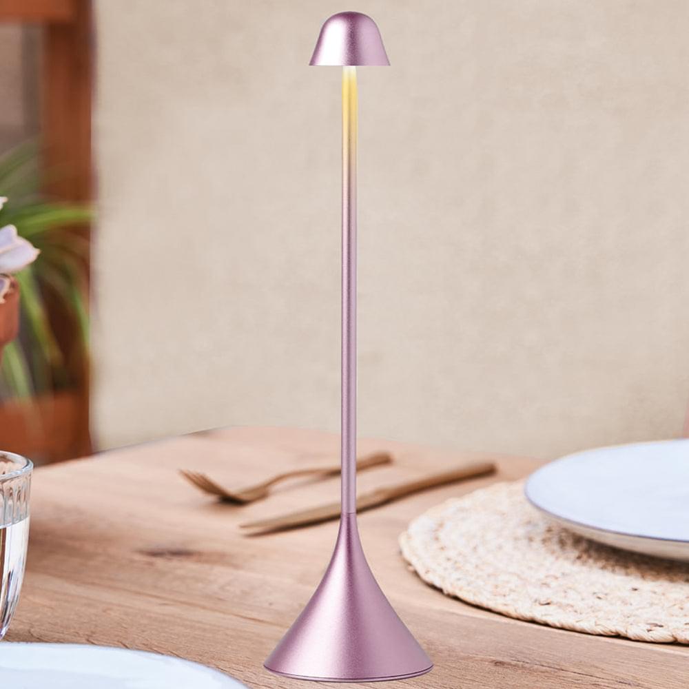Pink bell table lamp standing on base with soft warm light on.