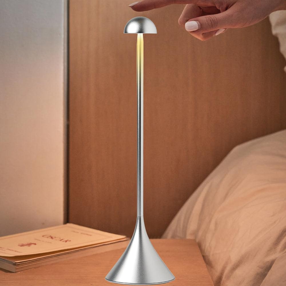 Polished aluminum table lamp with dome shade on tabletop, hand adjusting