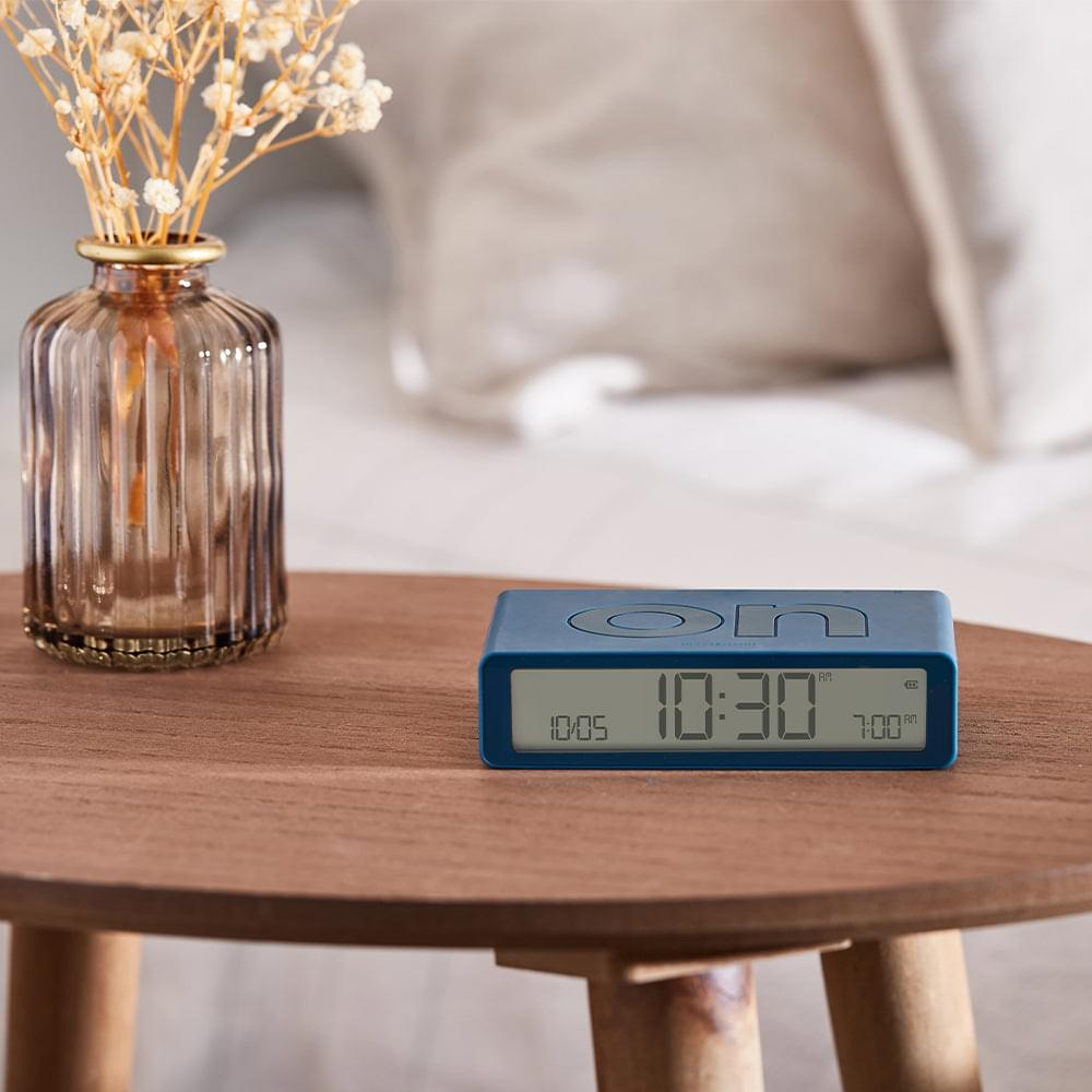 Blue reversible flip alarm clock on a wooden bedside table, showing time display
