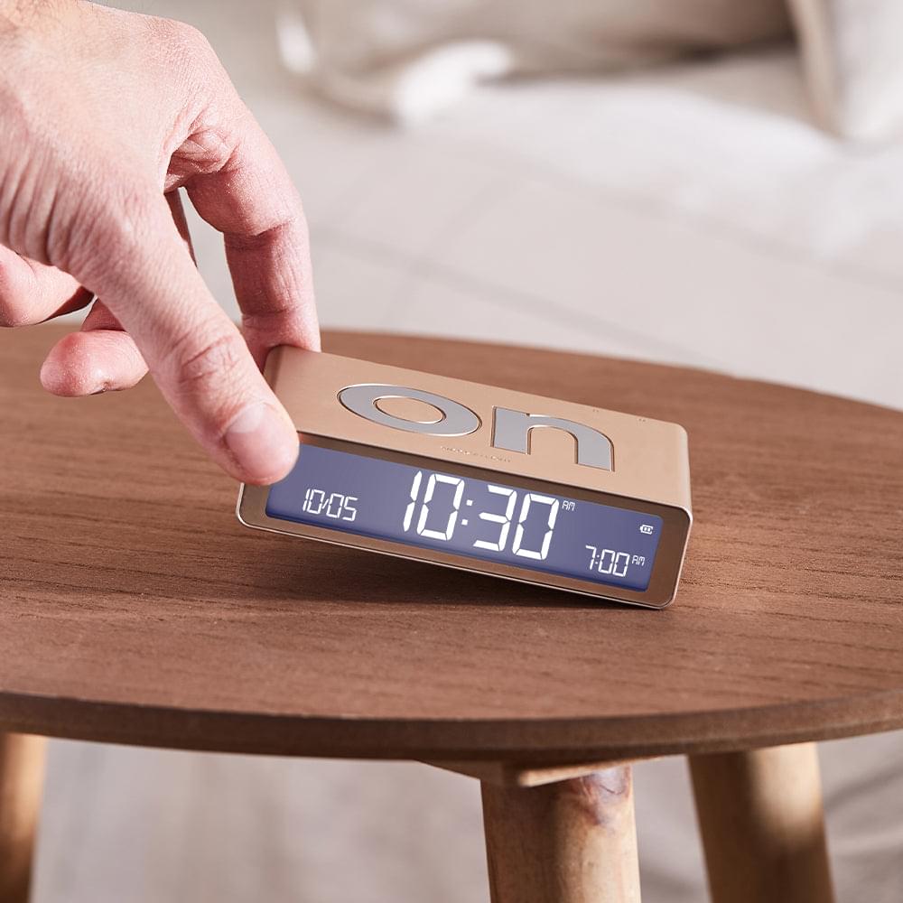 Gold alarm clock with blue digital display; hand pressing top controls