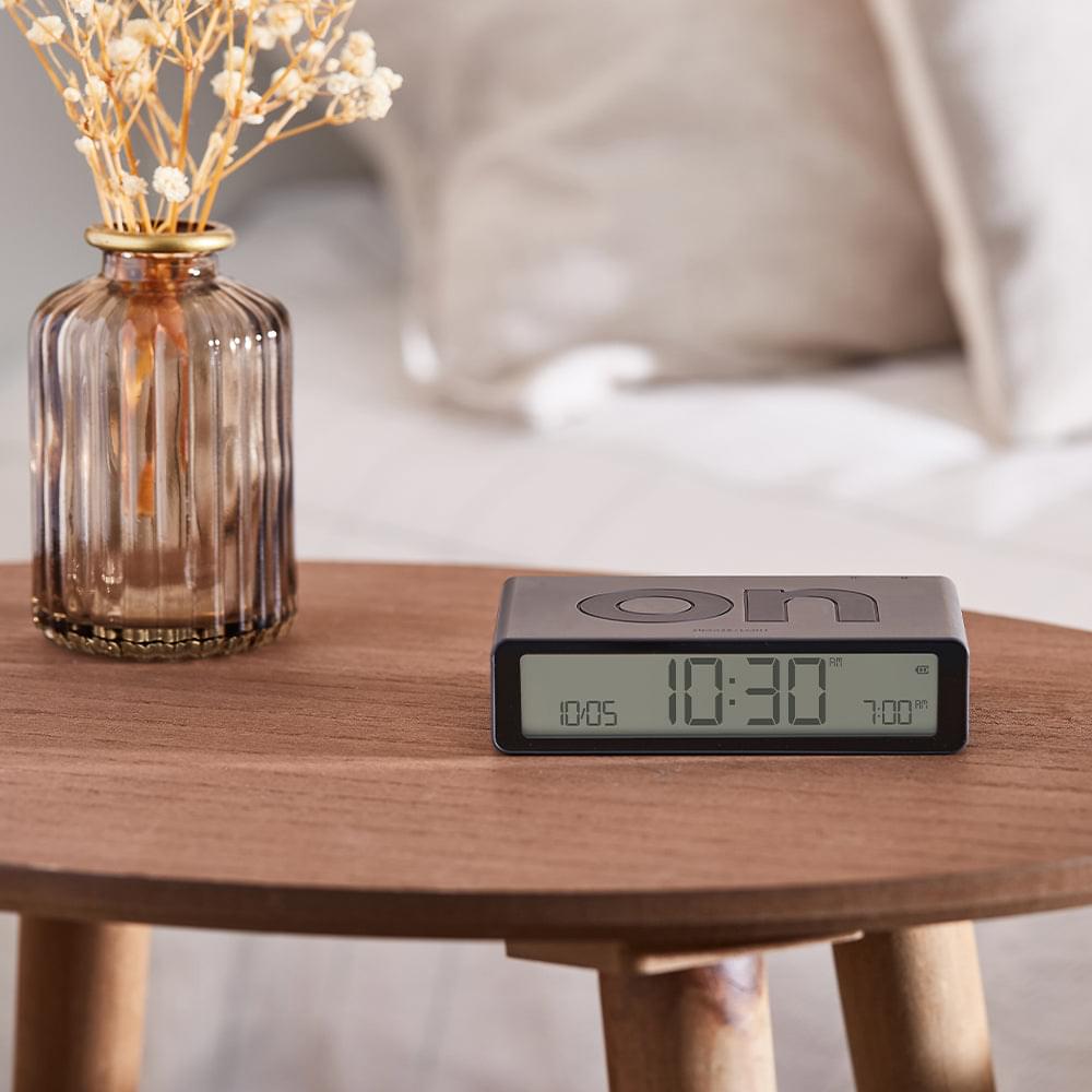 Grey flip alarm clock on a wooden table, LED display showing time and alarm time