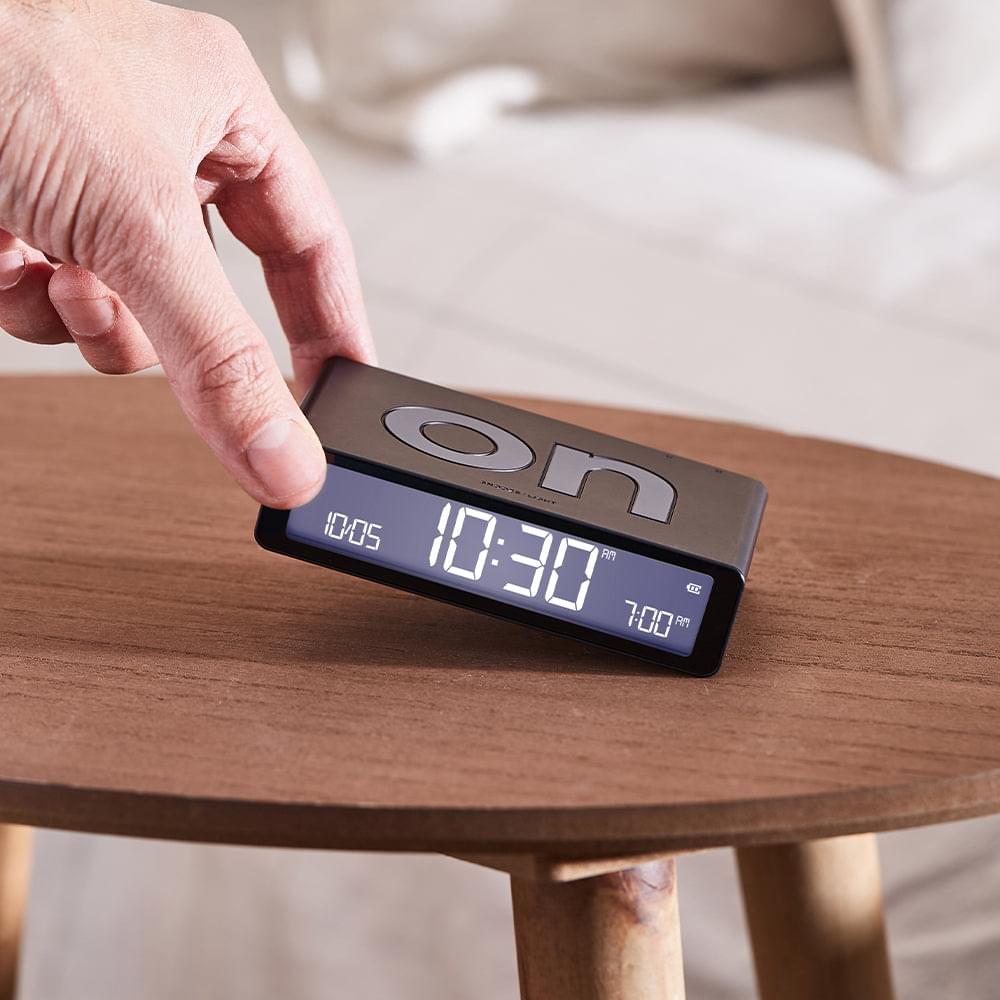 Black reversible alarm clock flipped by hand, glowing blue digital time display