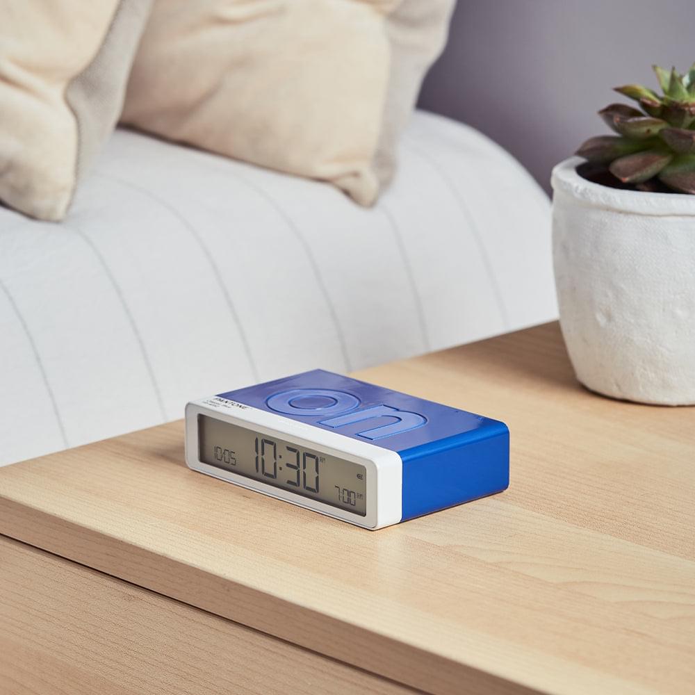 Blue flip alarm clock on a bedside table, LCD shows 12:31 and 100