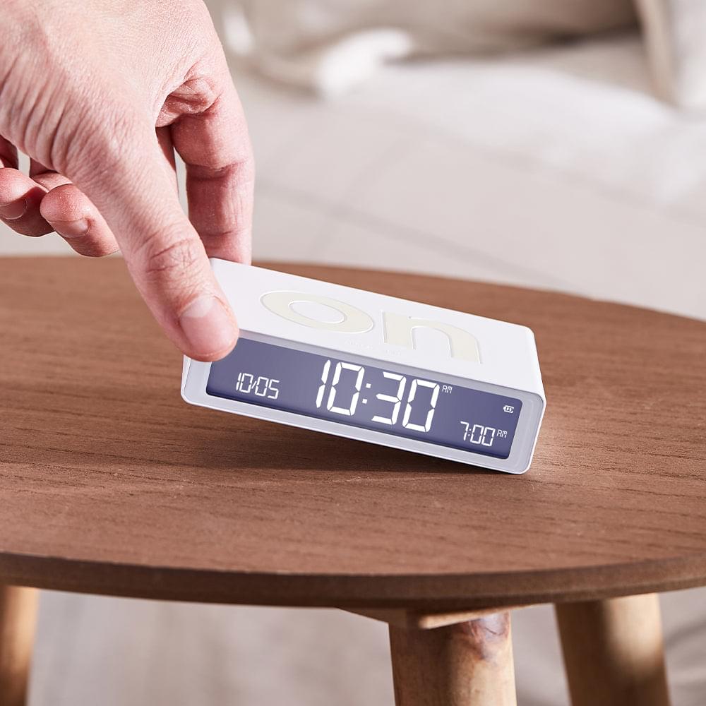 White reversible alarm clock with a hand pressing controls, LED time 12:30.