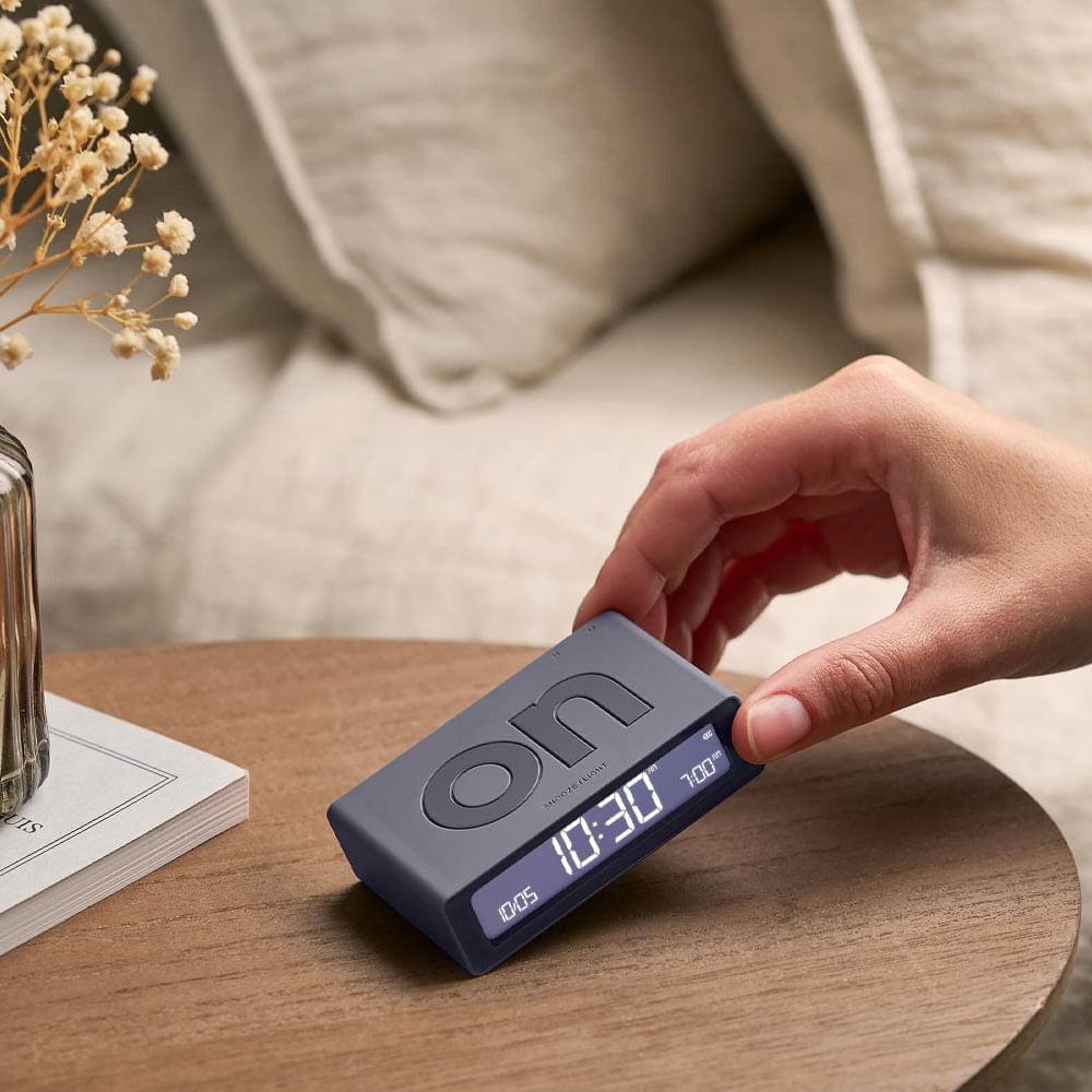 Grey flip mini reversible alarm clock with hand pressing the top buttons